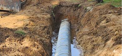 A large, blue pipe laid in a dirt trench partially filled with water.