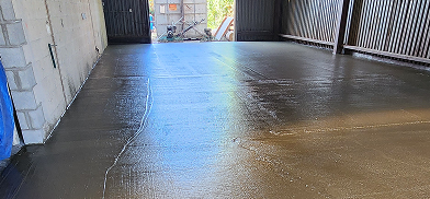 Newly poured, wet concrete floor in an indoor space, reflecting light from an open doorway.