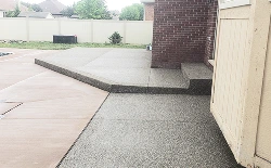 Raised gray speckled concrete patio with steps beside a building, connecting to an existing concrete slab.