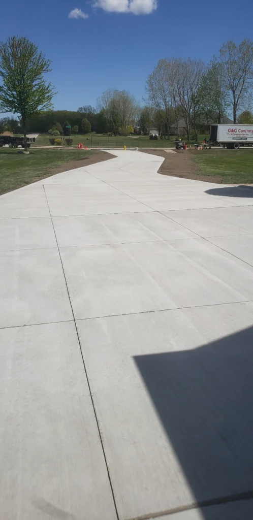 Freshly poured concrete driveway curves through a green lawn, with construction equipment and a G&G Concrete truck nearby.