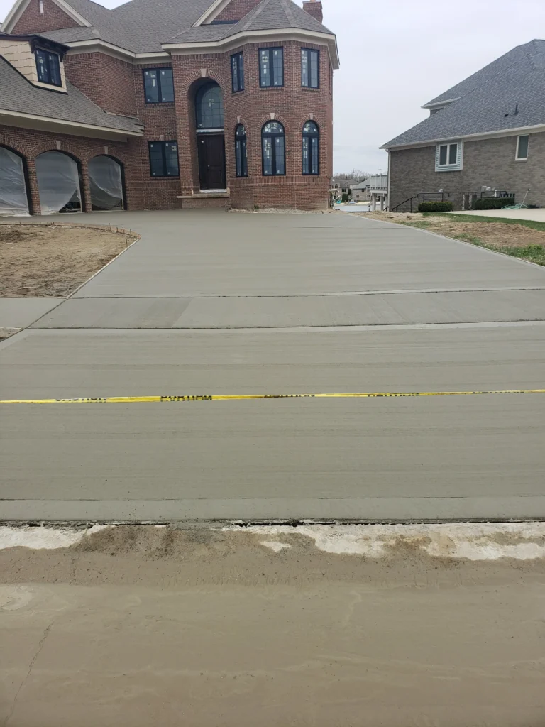 Freshly poured concrete driveway to a new brick house, with yellow caution tape blocking access.