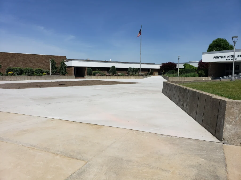 Fenton High School main entry and concrete plaza on a clear day, with an American flag and manicured landscaping.