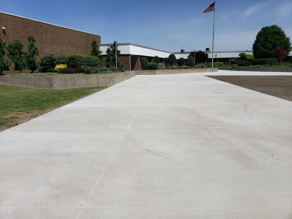 New concrete plaza leading to a brick building, surrounded by landscaping, with an American flag flying.