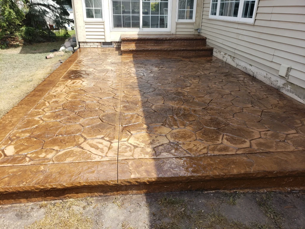 Wet, brown stamped concrete patio and two steps, patterned to resemble irregular flagstones.