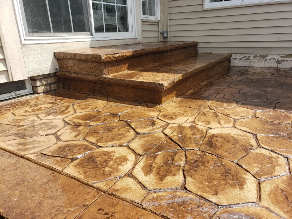 Wet, brown stamped concrete patio and two steps, patterned to resemble irregular flagstones.