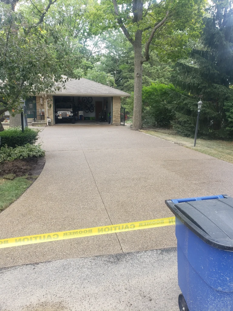 Single-story ranch house with a light-colored driveway leading to an open two-car garage revealing a dark Jeep. A basketball hoop, lamppost, and mature trees are in the front yard.