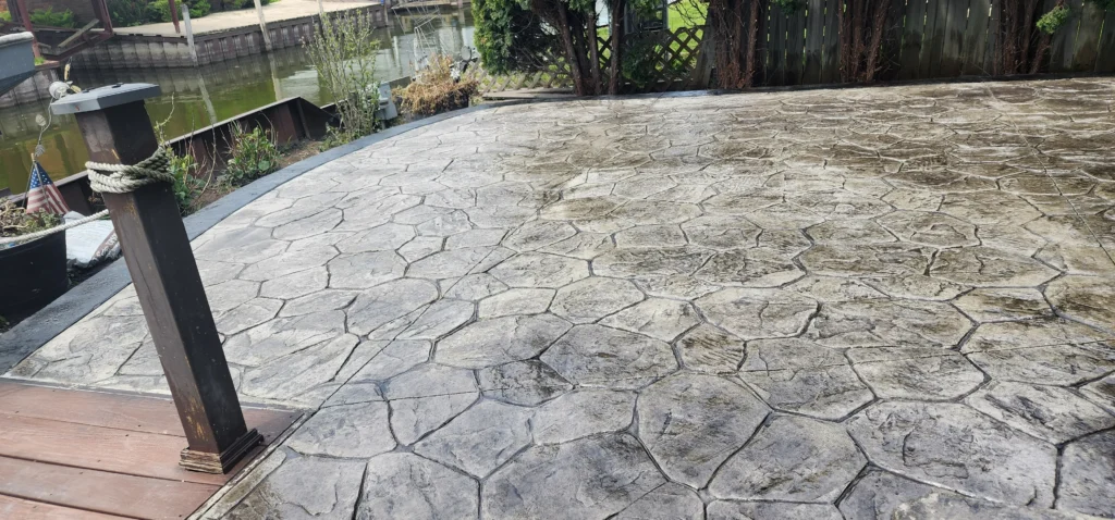 Wet, irregular stone-patterned concrete patio by a canal with docks and a wooden post with rope in the foreground.