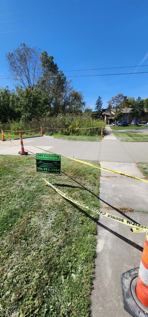 Newly poured concrete sidewalks and paths blocked by yellow caution tape and orange cones. G&G Concrete sign on grass.