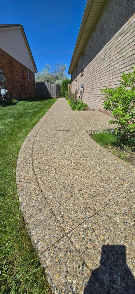 Concrete aggregate path curving between two houses with green grass under a clear blue sky.