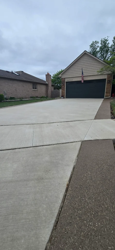 Freshly poured concrete driveway in front of a house with a two-car garage and American flag on a cloudy day.