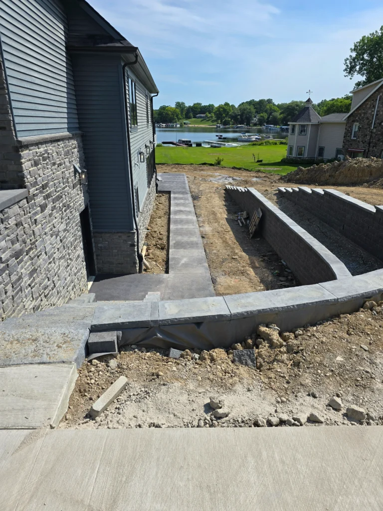 Lakefront home under construction with new stone retaining walls and pathways leading towards the lake with boats.