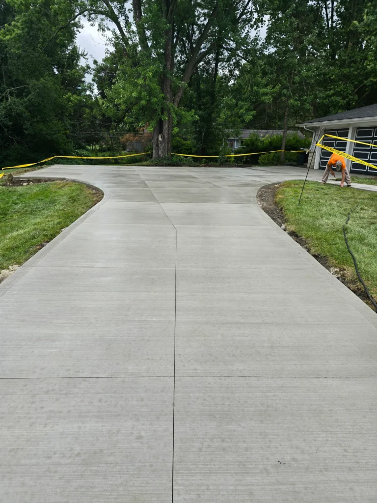 Freshly poured concrete driveway with a Y-split, bordered by grass and caution tape; a worker tends to the side.