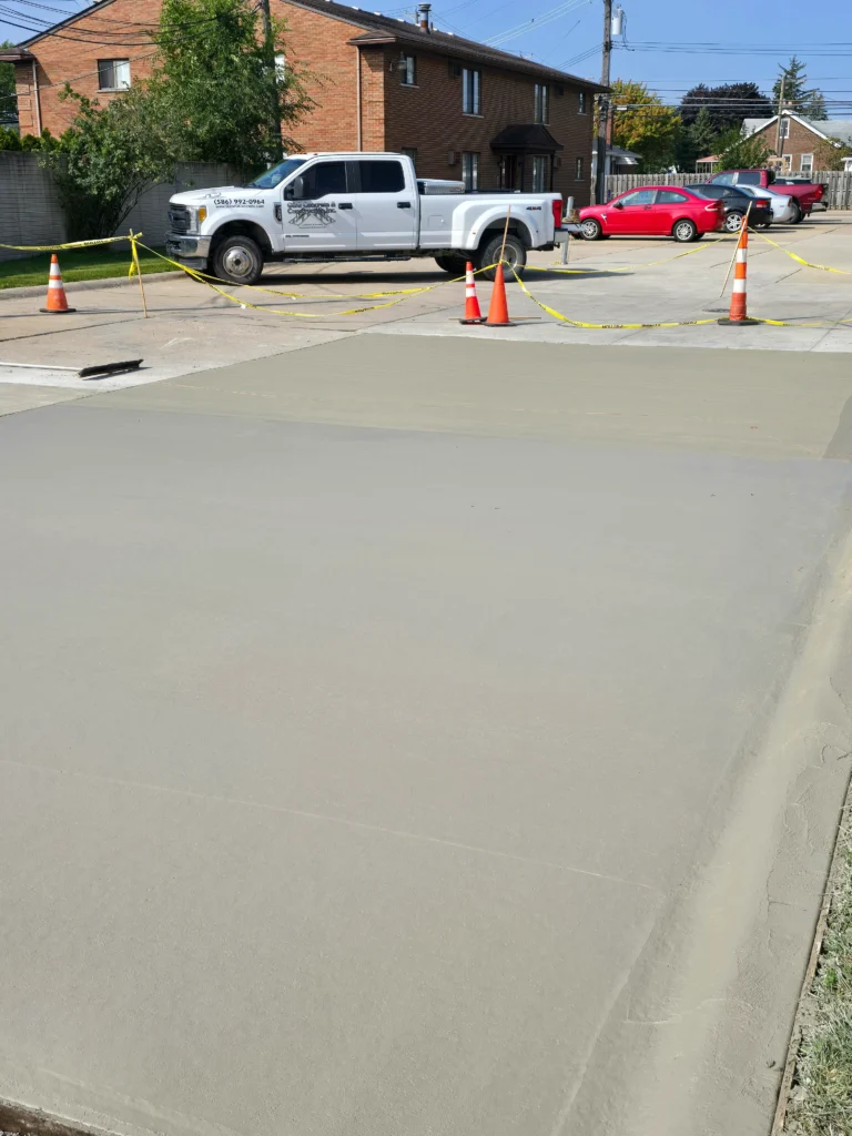 Newly poured concrete surface, marked with caution tape and cones, with a C&G Concrete truck beyond.