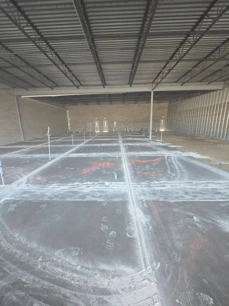Construction interior with dusty concrete floor showing footprints, exposed metal ceiling, block walls, and metal studs.