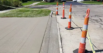 New concrete driveway protected by orange construction cones and yellow caution tape next to a grassy lawn.
