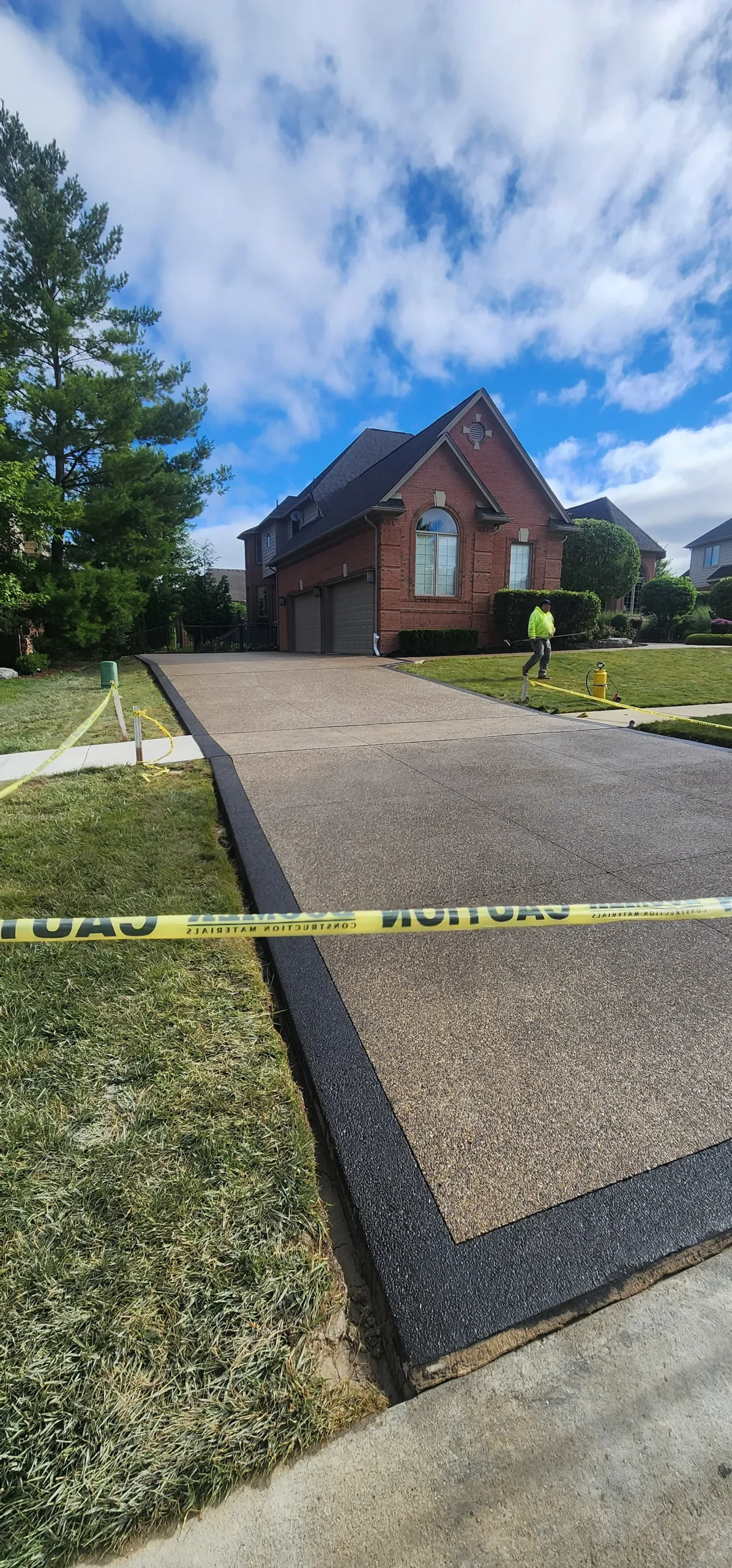 A long driveway made of exposed aggregate leading up to a large house, closed off with caution tape.