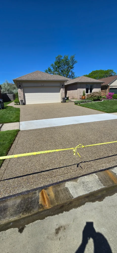 New aggregate concrete driveway with a freshly poured smooth concrete section, cordoned off by yellow caution tape.