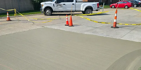 Freshly poured concrete driveway sectioned off with safety cones and yellow caution tape near a white pickup truck.