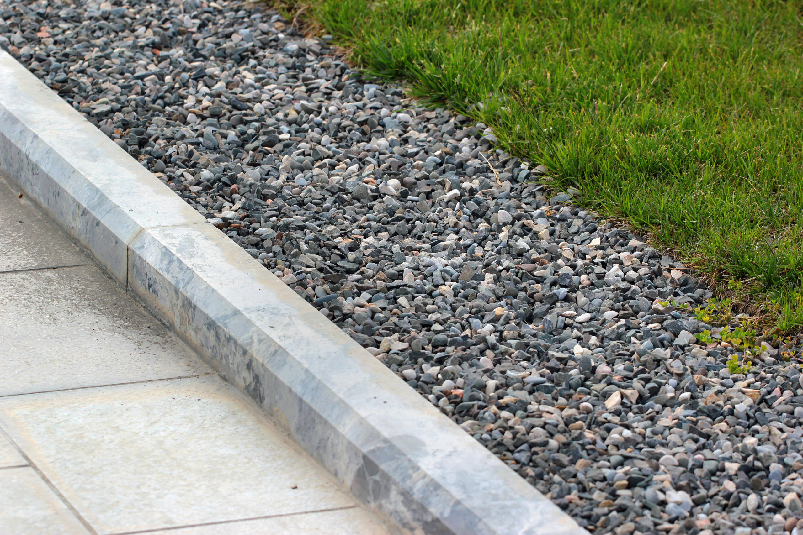 A concrete curb, decorated with gray and white marbling, is constructed in front of gravel and grass.
